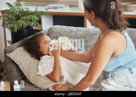 Fürsorgliche, liebevolle und besorgte Eltern, die sich um kranke Kinder kümmern. Erkältung, Grippe oder Covid-Virus. Tochter, Kind und krankes Mädchen liegen auf dem Sofa Stockfoto