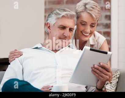 Ein reifes Paar, das ein digitales Tablet zu Hause auf dem Sofa zusammen benutzt. Stockfoto
