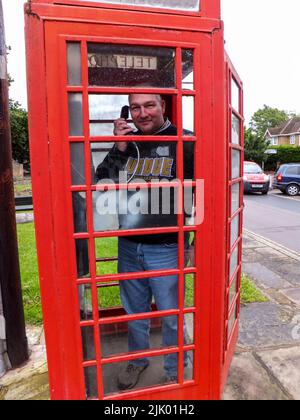 Ein Mann, der in einer berühmten roten Telefonzelle in Harmondsworth, Hillingdon, Middlesex, London, England, einen Anruf macht, VEREINIGTES KÖNIGREICH. Stockfoto