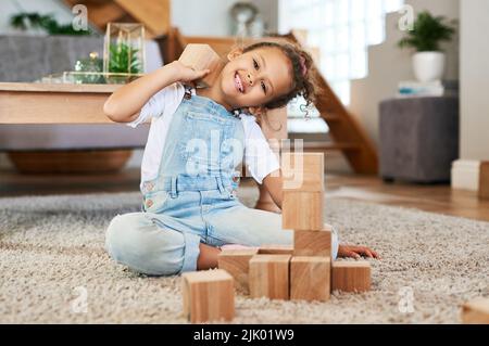 Spielzeit ist die beste Zeit. Portrait eines entzückenden kleinen Mädchens, das zu Hause mit Holzblöcken spielt. Stockfoto