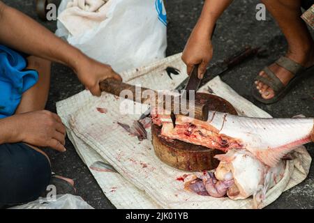 Ein Händler schneidet den Fisch mit einem Messer zum Verkauf in Stücke. In einem der Morgenmärkte in Thailand. Stockfoto