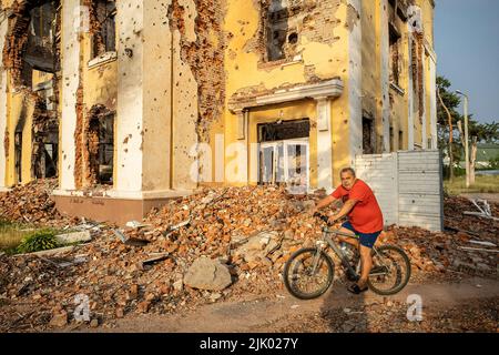 Ein Mann auf dem Fahrrad fährt an den Ruinen einer Schule in Charkiw vorbei. Charkiw gilt als zweitgrößte Stadt der Ukraine, war eines der wichtigsten strategischen Ziele der russischen Invasion und seit Kriegsbeginn hat die Stadt mehrere Raketenangriffe erlitten, da die Beamten die Stadt als "Heldenstadt der Ukraine" bezeichneten. Stockfoto