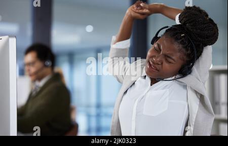 Jeder verdient eine Pause. Eine junge Callcenter-Agentin, die sich bei der Arbeit in einem Büro ausstreckt. Stockfoto