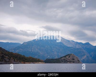 Reise zur Lagune in Oludeniz, Fethiye, Türkei. Strand in der Nähe von Darbogaz. Mit Blick auf den Berg Babadag, Winterlandschaft mit Bergen, grünem Wald, azurblauem Wasser, Strand und bewölktem Himmel Stockfoto