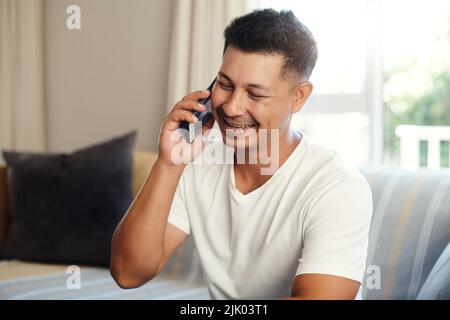 Ein hübscher junger Mann, der alleine auf dem Sofa zu Hause sitzt und sein Handy benutzt. Stockfoto