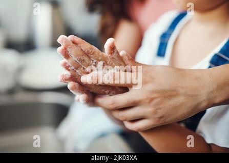 Halten Sie diese Hände keimfrei. Eine unkenntliche Frau hilft ihrer Tochter, sich die Hände im Küchenwaschbecken zu Hause zu waschen. Stockfoto