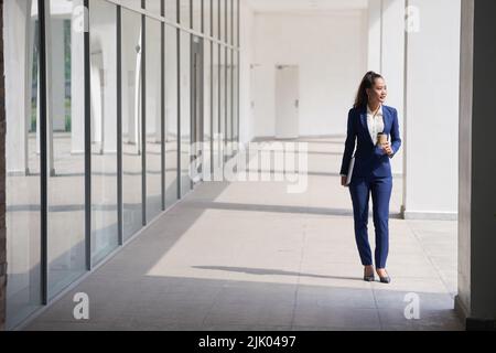 Geschäftsfrau mit einer Tasse Kaffee zum Mitnehmen geht zur Arbeit Stockfoto