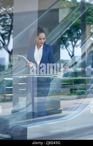 Asiatische junge Geschäftsfrau geht die Rolltreppe hinunter Stockfoto