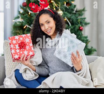 Alle diese Geschenke, aber ich bin immer noch das beste Geschenk. Eine junge Frau hält Geschenke während der Weihnachtszeit zu Hause. Stockfoto