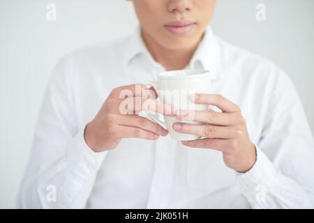 Beschnittenes Bild eines jungen Mannes, der eine Tasse Tee in der Hand hält Stockfoto