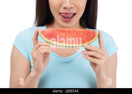 Nahaufnahme einer unkenntlichen Frau, die ihre Lippen leckt, während sie eine saftige Wassermelone in den Händen hält, isoliert auf weißem Hintergrund Stockfoto