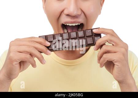Nahaufnahme eines nicht erkennbaren Mannes, der ein gelbes T-Shirt trägt und eine Schokolade beißt, während er vor weißem Hintergrund steht Stockfoto