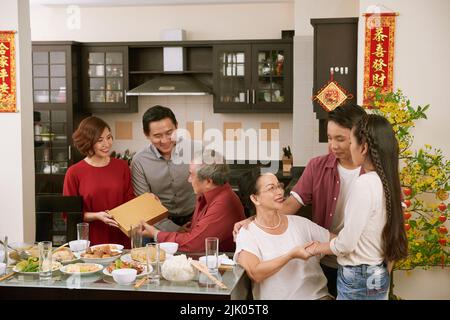 Große vietnamesische Familie feiert das Frühlingsfest zu Hause. Schriftrollen, die Glück und Reichtum im Hintergrund wünschen Stockfoto