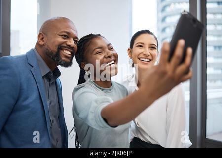 Eine Gruppe von Geschäftsleuten, die zusammen Selfies in einem Büro machen, strahlt Vertrauen durch sie alle. Stockfoto