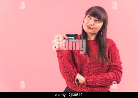 Schöne reife Frau mit langen braunen Haaren, die gerne mit Kreditkarte einkaufen und darüber nachdenken, was sie kaufen soll. Hochwertige Fotos Stockfoto