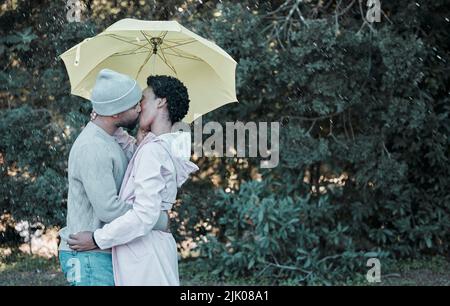 Die besten Küsse sind die, die im Regen geteilt werden. Ein junges Paar küsst sich unter einem Regenschirm. Stockfoto