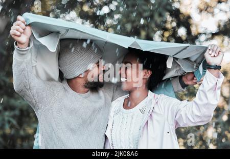 Nicht einmal der Regen kann mich von Euch fernhalten. Ein junges Paar, das draußen im Regen eine Jacke über ihren Köpfen hält. Stockfoto