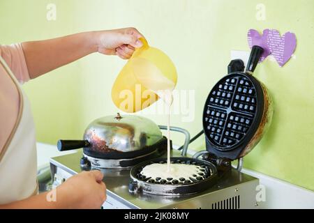 Zugeschnittenes Bild einer Frau, die Teig in den Waffeleisen gießt Stockfoto