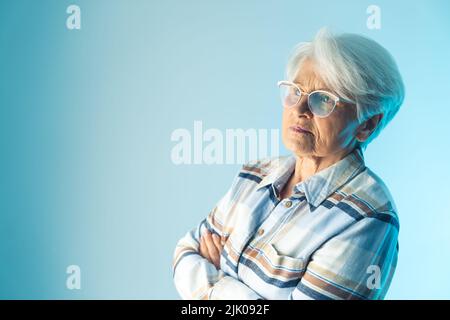 Ältere, pensionierte, kurzhaarige Frau blickt mit gekreuzten Armen nachdenklich weg und reflektiert über Erinnerungen oder denkt über etwas nach. Hochwertige Fotos Stockfoto