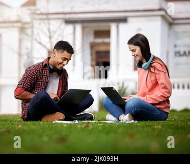 Wir helfen uns immer gegenseitig. Zwei Studenten benutzen ihre Laptops, während sie draußen auf dem Campus sitzen. Stockfoto