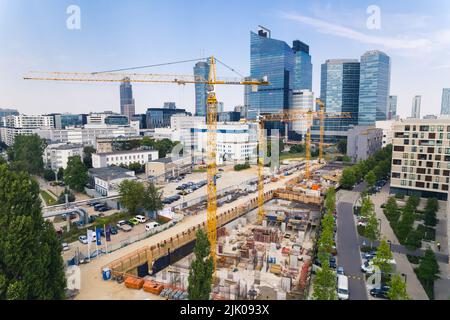 7.22.2022 Warschau, Polen. Vier gelbe Baukräne auf einer riesigen Baustelle arbeiten an einem neuen Projekt. Wolkenkratzer im Hintergrund. Neues Immobilienkonzept. Hochwertige Fotos Stockfoto