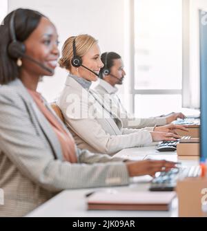 Auf Abruf und bereit zu helfen. Eine attraktive, reife Callcenter-Agentin, die ein Headset trägt, während sie mit ihren Kollegen im Büro arbeitet. Stockfoto