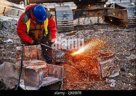 Ein Mitarbeiter im Helm schneidet alte Metallbalken für das Recycling vor Ort Stockfoto