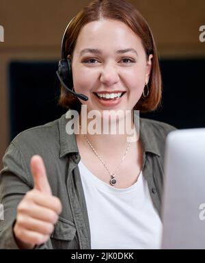 Ein junger Callcenter-Agent sitzt allein im Büro und macht eine Geste mit dem Daumen nach oben. Stockfoto