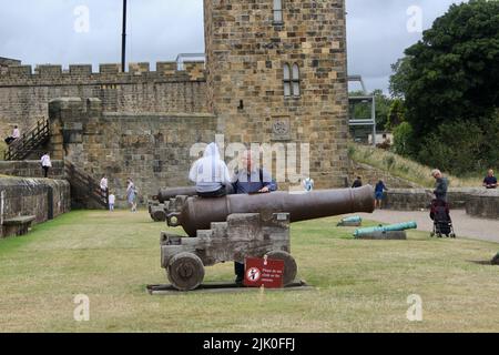 Kind sitzt auf einer Kanone mit einem nicht auf Kanonen sitzen Zeichen alnwick england Großbritannien Stockfoto