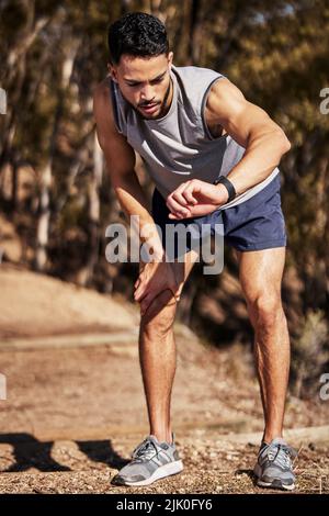 Wie war meine Zeit heute. Ganzkörperaufnahme eines hübschen jungen Mannes, der während seines Laufs im Freien auf seine Uhr schaut. Stockfoto