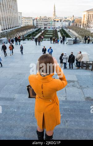 Dame in einem orangefarbenen Mantel, die das Stadtbild von Brüssel vom Mont des Arts fotografiert Stockfoto