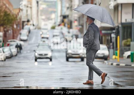 Bei diesem Wetter möchte ich im Bett bleiben. Ein hübscher Geschäftsmann, der an einem regnerischen Tag zur Arbeit geht. Stockfoto
