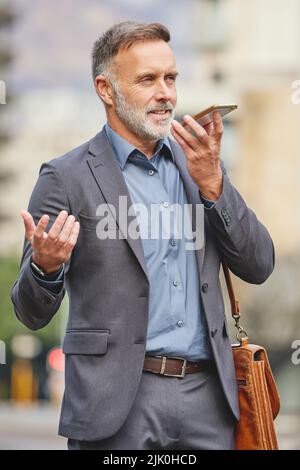 Ich denke, diese Pläne müssen einige Änderungen. Ein reifer Geschäftsmann mit seinem Smartphone, um eine Sprachaufnahme zu senden. Stockfoto