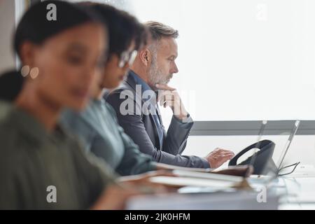 Denken Sie an die beste Lösung. Ein reifer Geschäftsmann, der zusammen mit seinen Kollegen in einem Callcenter an einem Laptop arbeitet. Stockfoto