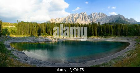 Atemberaubender Panoramablick auf den Karersee (Lago di Carezza) mit seinem smaragdgrünen Wasser, wunderschönen Bäumen und Bergen in der Ferne. Stockfoto