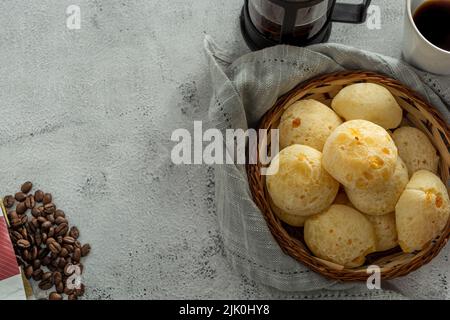 Korb mit Käsebrot oder 'pao de queijo, mit Kaffeeartikeln, auf einem Steintisch Stockfoto
