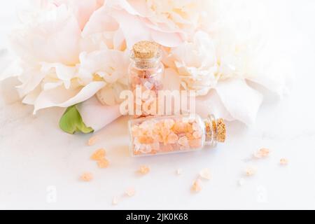 Beauty- und Spa-Konzept. Rosafarbenes himalaya-Salz in Nahaufnahme in Glasboteln, ätherisches Öl und Pfingstrose im Hintergrund. Selektiver Fokus. Stockfoto
