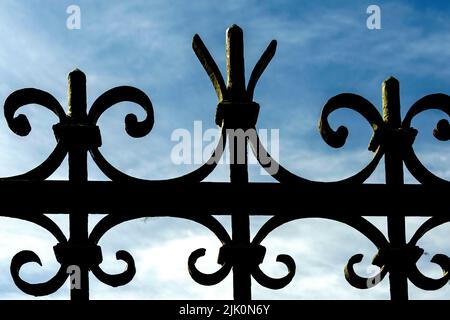 Aus nächster Nähe einen schmiedeeisernen Zaun mit verzierten lockigen Mustern vor einem hellblauen Himmel. Stockfoto