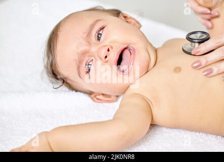 Wann kommen wir hier raus. Ein kleines Baby, dessen Brust von einer Ärztin untersucht wird. Stockfoto