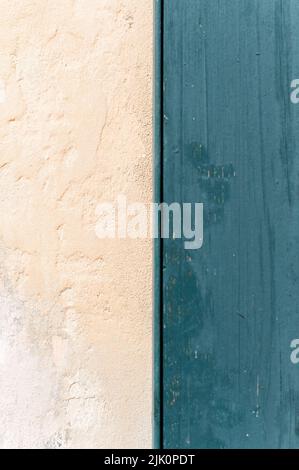Eine vertikale Nahaufnahme einer schlichten cremefarbenen Wand, die auf eine blaue Holztür trifft Stockfoto