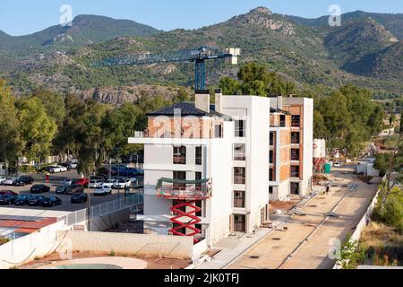 Gebäude. Gebäude im Bau mit einem Kran. Bergige Landschaft im Hintergrund. Horizontale Fotografie. Stockfoto