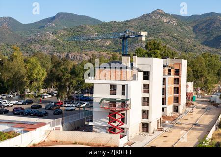 Gebäude. Gebäude im Bau mit einem Kran. Bergige Landschaft im Hintergrund. Horizontale Fotografie. Stockfoto