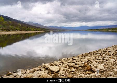 Sumpflandschaft mit Reflexen im Wasser der Berge und Ufer mit großen rustikalen Steinen. Lozoya Madrid. Stockfoto
