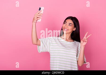 Foto von entzückenden jungen koreanischen Frau halten Gadget zeigen V-seufz Selfie Video-Anruf tragen stilvolle weiße Kleidung auf rosa Hintergrund isoliert Stockfoto