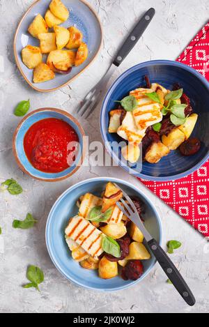 Spanisches Abendessen mit gebackenen Kartoffeln, gegrilltem Halloumi, gebratenem Chorizo und Tomatensauce Stockfoto