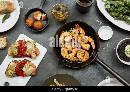 Garnelen in einer Pfanne mit Knoblauch und Petersilie und mehreren anderen Gerichten auf dem Tisch Stockfoto