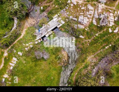 Luftaufnahme einer Frau, die auf einer alten Steinbrücke im grünen Feld liegt. Spanien. Stockfoto