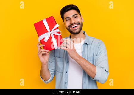 Foto-Porträt von schönen glücklich hispanischen Geburtstag Kerl Hände halten giftbox gekleidet stilvolle Jeans aussehen isoliert auf gelbem Hintergrund Stockfoto