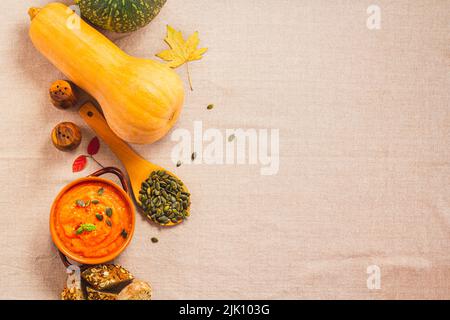 Kürbis- und Karottensuppe in Tonschüsseln und Bio-Kürbisse mit schwarzem Brot auf Leinenhintergrund. Vegetarische Herbstsahnesuppe aus Kürbis mit Samen. Stockfoto