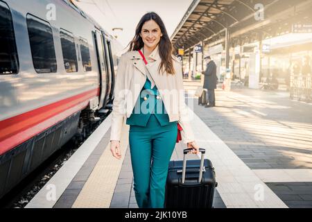 Porträt einer Geschäftsfrau, die mit Handgepäck in einem Bahnhof oder Flughafen zum Boarding Gate geht Stockfoto